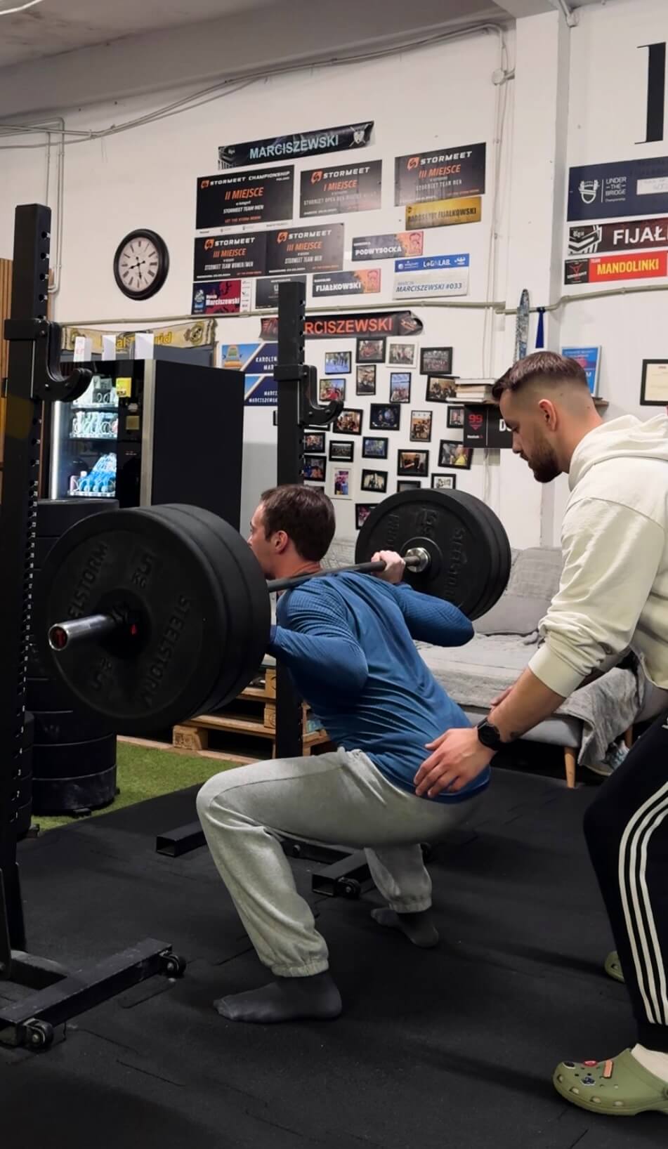 Podopieczny wykonujący przysiad ze sztangą pod okiem trenera osobistego z Warszawy